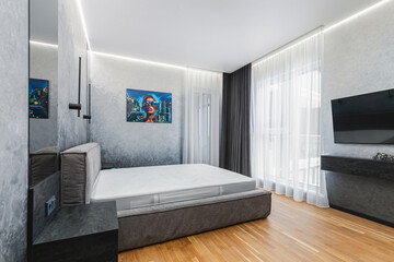 A contemporary bedroom features a large, unmade bed against a stylish gray wall. Bright curtains...