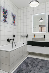 This contemporary bathroom showcases a sleek bathtub, stylish mirror, and modern sink, all nestled within a clean, minimalist design. The black accents enhance its elegance.