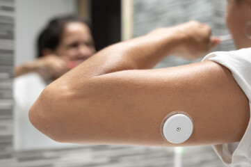 Woman brushing teeth with continuous glucose monitoring sensor on arm