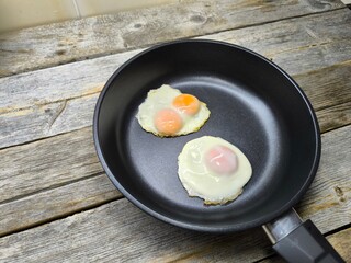 Two fried eggs in a black frying pan on a wooden table