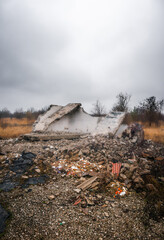 An old, destroyed concrete bus stop with bricks and other debris scattered around it, against a stormy sky