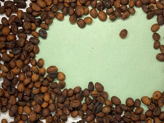 Brown roasted coffee beans frame on green  paper