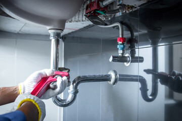 Plumber hands holding wrench doing repairing work at the sink and clogged pipe in bathroom carefully