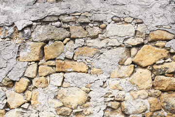 Old stone wall background. Rough surface of mixed stones and cement. Natural gray and yellow texture. Rustic uneven construction detail. Weathered exterior of vintage traditional architecture.