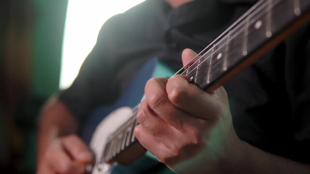 A low-angle close-up shot focusing on a man&rsquo;s hands and guitar. Backlighting adds mood and dimension while a soft key light keeps surface detail visible. No face included.