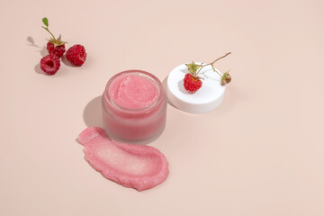 A jar of natural body scrub, a swatch of scrub and raspberry berries on a beige background