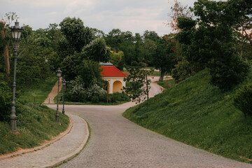 Curving cobblestone road with vintage street lamps and a yellow building in the green surroundings of Petrovaradin Fortress, Novi Sad, Serbia
