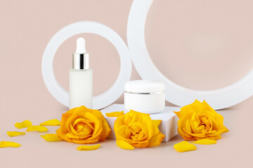 A set of cosmetics, creams and serums. White glass bottles on a beige background with yellow rose flowers. Rejuvenation and hydration.