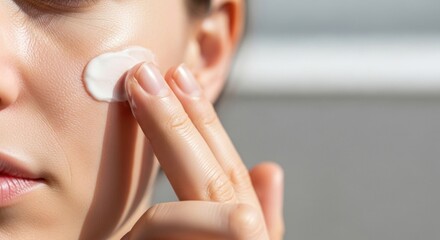 Woman applying white cream to her cheek with two fingers in bright light