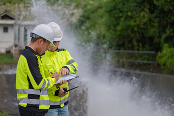 A engineering doing his checking routine. He is wearing hard hat and engineer uniform.Standing by the rail by the dam.Monitor water levels from the heavy rain that has been falling for several days.