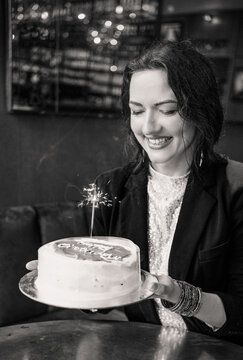 Smiling woman holding a birthday cake with a sparkler