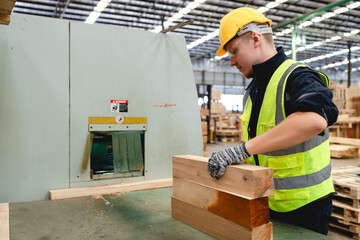 Industrial employee placing wooden beams into machinery for trimming in organized warehouse, enhancing timber precision for pallet production and construction material.
