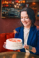 Smiling woman holding a birthday cake with a sparkler