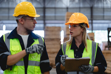 Male and female logistic employees wearing safety equipment discuss operation tasks in spacious warehouse setting, Team communication concept.