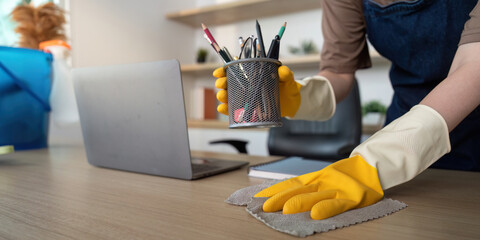 Home Cleaning. Woman holding a pen holder while cleaning her desk in a modern workspace.