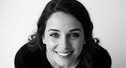 A black and white portrait of a woman with dark hair smiling directly at the camera with a bright background