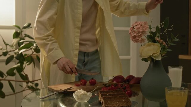 Midsection shot of unknown woman putting smartphone on glass table and cutting tomatoes on wooden board, pre-teen son stealing off red apple