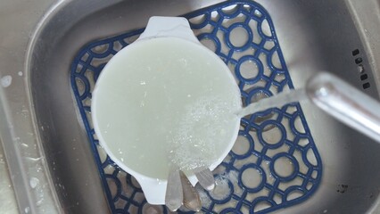 Washing white dish with liquid under water stream in sink, highlighting kitchen cleaning process