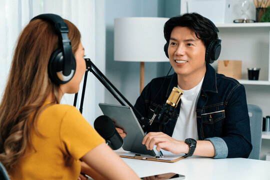Smiling radio influencer host holding tablet wearing headphones interview woman speaker social media online live streaming channel with talking to share link at morning at studio record. Infobahn. - Powered by Adobe