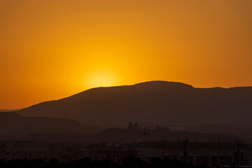 Sunset over the scenic hills of Alicante reveals vibrant orange hues against a tranquil sky,...