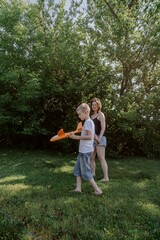 Fototapeta premium A mother and her son with hearing aids launch a paper airplane in a park, a heartwarming moment of inclusive play and bonding in nature. Perfect for disability awareness and family lifestyle content