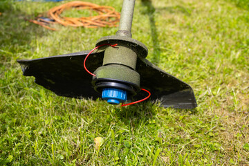 The electric lawn mower stands on the green grass. the power cord is twisted into a spiral.
