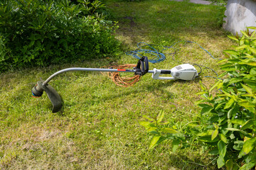 The electric lawn mower stands on the green grass. the power cord is twisted into a spiral.