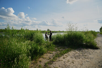 Friends explore a serene lakeside in the afternoon surrounded by lush greenery and a clear sky