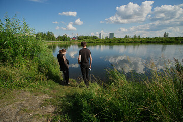 Two men walking along a gravel path in a green park on a sunny day with blue skies and clouds in the background