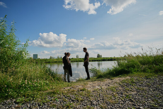 Two men walking along a gravel path in a green park on a sunny day with blue skies and clouds in the background