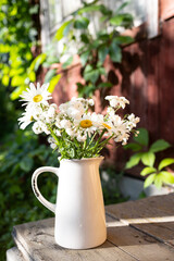 Gypsophila and daisies in a white vase on the grass. Country sunset