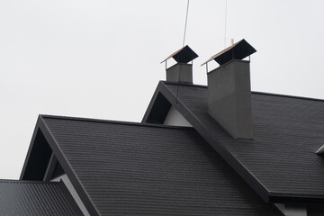Rooftops of a contemporary home with sleek, dark shingles and prominent chimneys stand out against...
