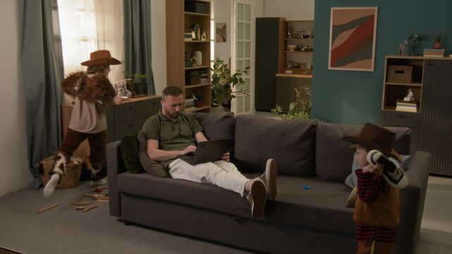 Elder child jumping on couch where his father working on laptop, younger kid aiming toy gun at brother and throwing sneaker, mother appearing and taking sons away
