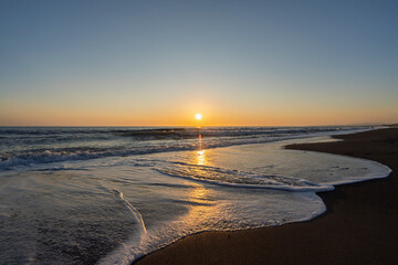 golden sunset over the Mediterranean Sea with small waves on sandy beach in Marina di Bibbona in...