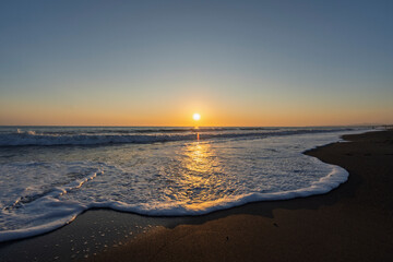 golden sunset over the Mediterranean Sea with small waves on sandy beach in Marina di Bibbona in Tuscany in Italy