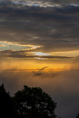 golden sunset over the clouds or fog of tuscany in a view from Montepulciano into the backlight of the going sun with silhouettes of trees