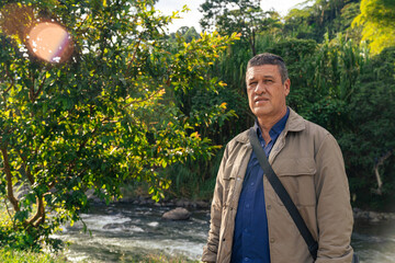 Older man standing in lush Colombian forest with river and sunlight in background