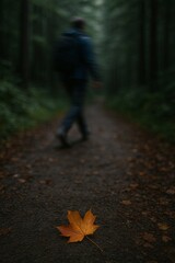 A solitary autumn leaf on a forest path with a person walking away in the background
