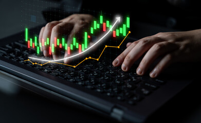 A close-up view of hands working on a laptop keyboard with an overlay of a stock market chart, showing dynamic candlestick patterns indicating market movements. Impute