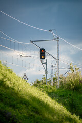 Modern railway traction system with red signal light, set against vibrant green grass and a...
