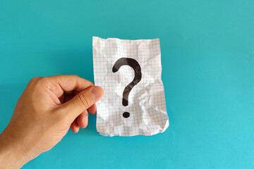 Question mark design. Hand holding a question mark on a crumpled paper against a blue background.