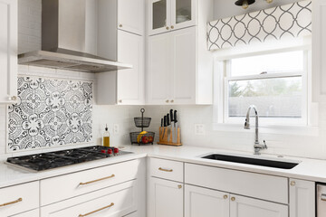 A kitchen detail with white cabinets, gold hardware, pattern accent tile under the range hood, subway tile backsplash, and white marble countertop.