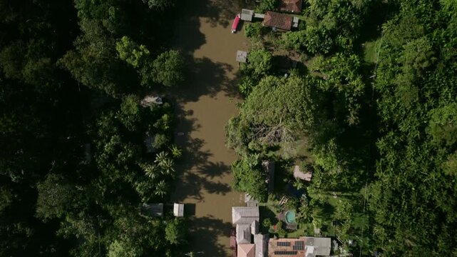 Aerial view of a boat travelling along a riverside village in the amazon rainfores in Brazil - Drone shot from an amazon rainforest and river