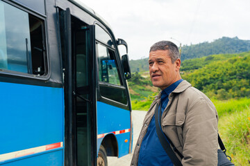 Man standing next to a bus on a rural road surrounded by lush countryside and a communications...