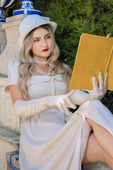Beautiful young blonde model wearing a glamorous vintage-inspired ivory dress, long satin gloves,...