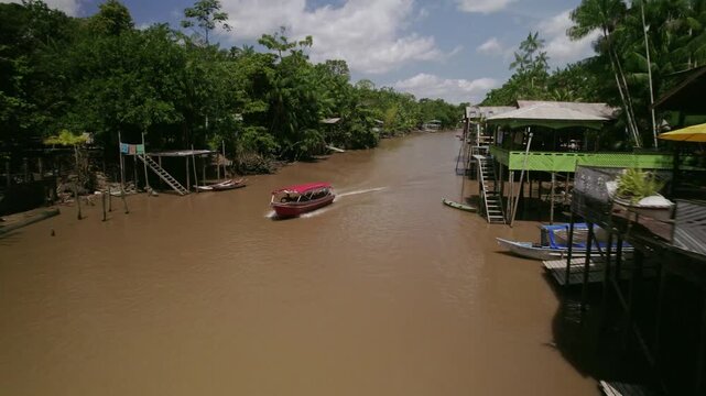 Aerial view of a boat travelling along a riverside village in the amazon rainfores in Brazil - Drone shot from an amazon rainforest and river