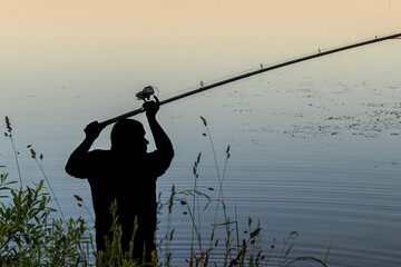 Fishing at dawn with a silhouette against tranquil waters during a calm morning by the lake