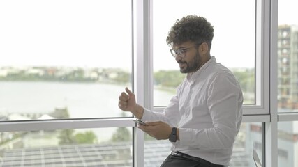 Young professional, focused, sitting by the window, using his smartphone - Powered by Adobe