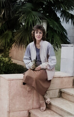 Vintage portrait of a pretty middle-aged woman sitting near a palm tree. Retro 1985.