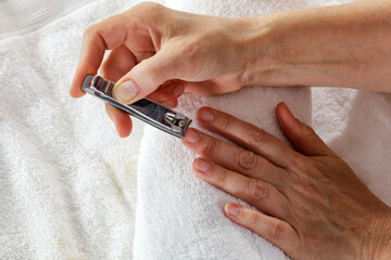 Elderly woman taking care of herself by doing her own manicure of damaged hands and broken nails at home. Close-up of hands during the beauty routine. Natural light and cozy home spa.